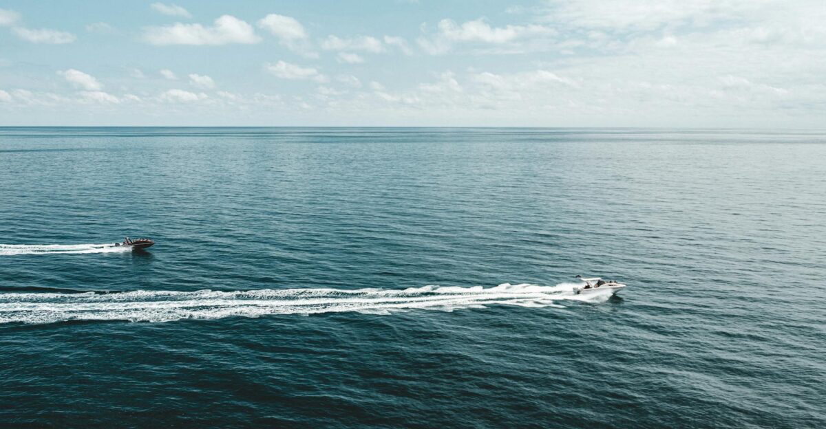 Aerial view of speedboats racing across vast open ocean under a sunny sky