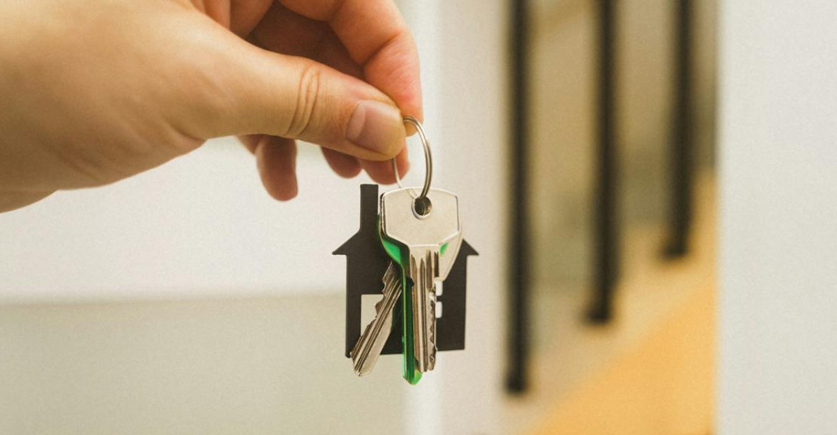 A hand holding a house key indoors signifies new ownership or leasing in real estate
