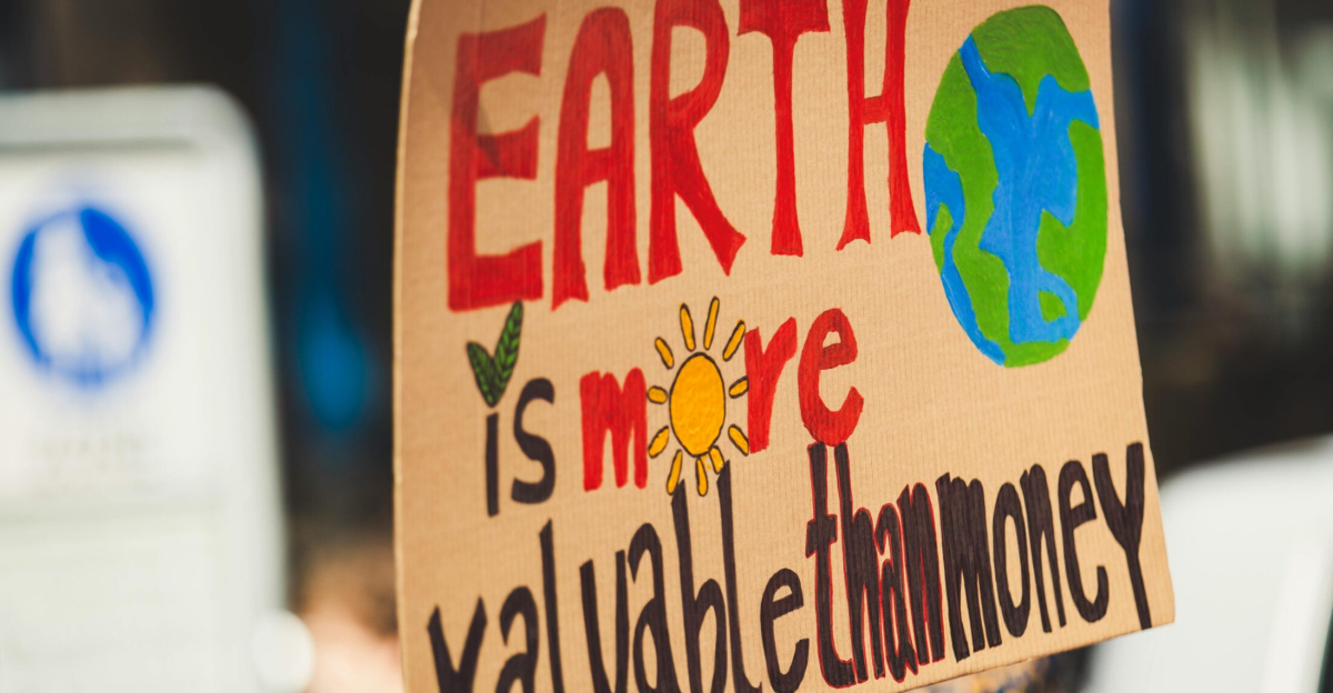 Sign reading 'Earth is more valuable than money' at a climate protest outdoors.