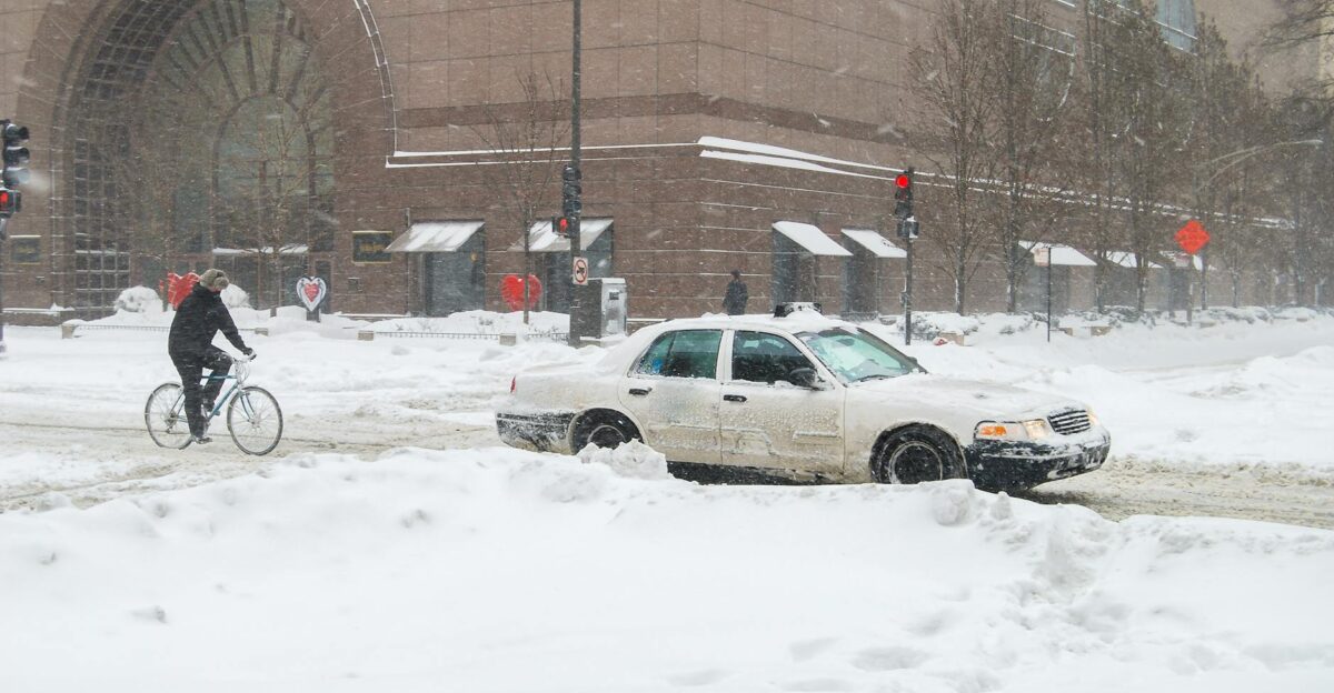 Snowy Chicago street scene featuring a cyclist and a car amidst winter snowfall