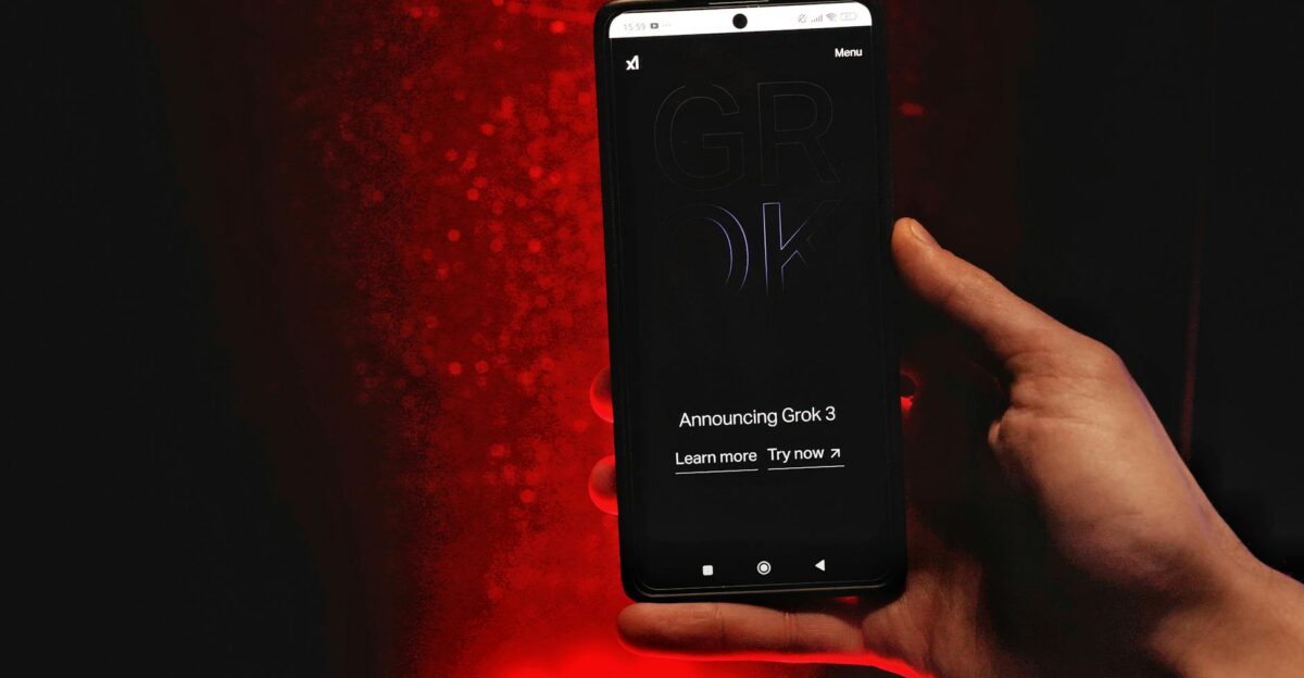 A hand holds a smartphone displaying Grok 3 announcement against a red background