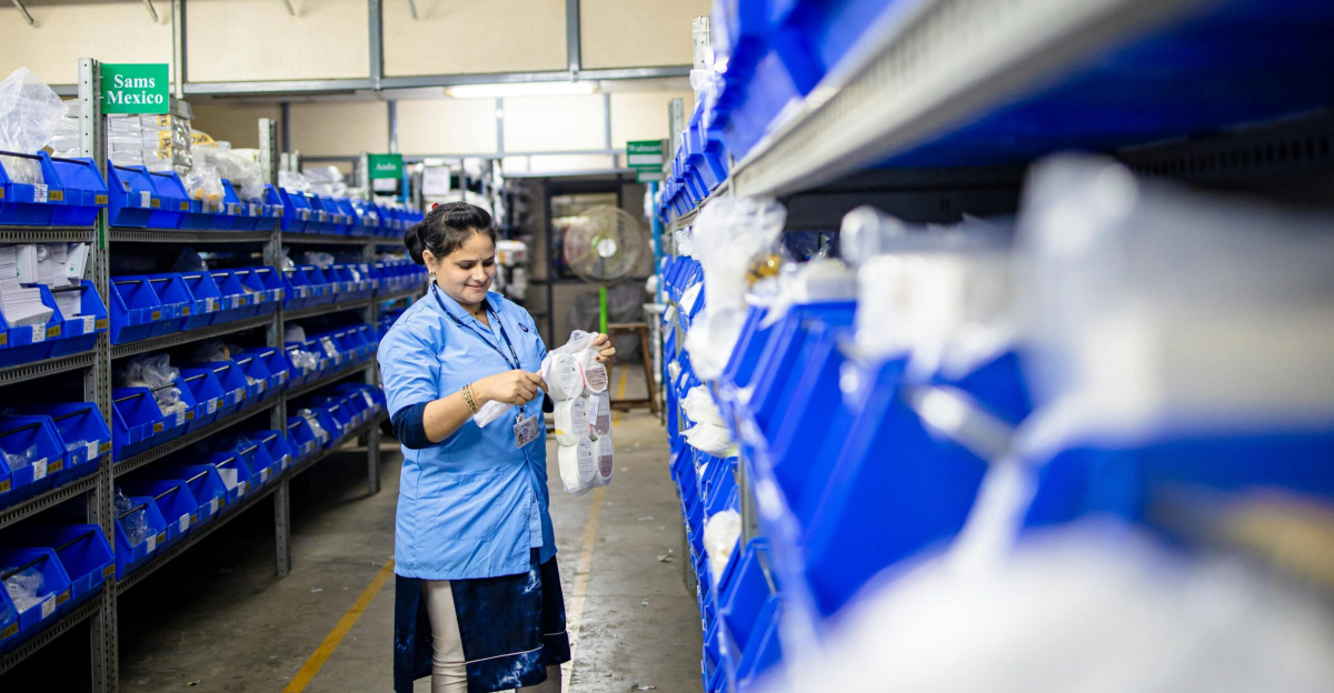 Female worker organizes shelves in a warehouse. Industrial setting with labeled storage bins.