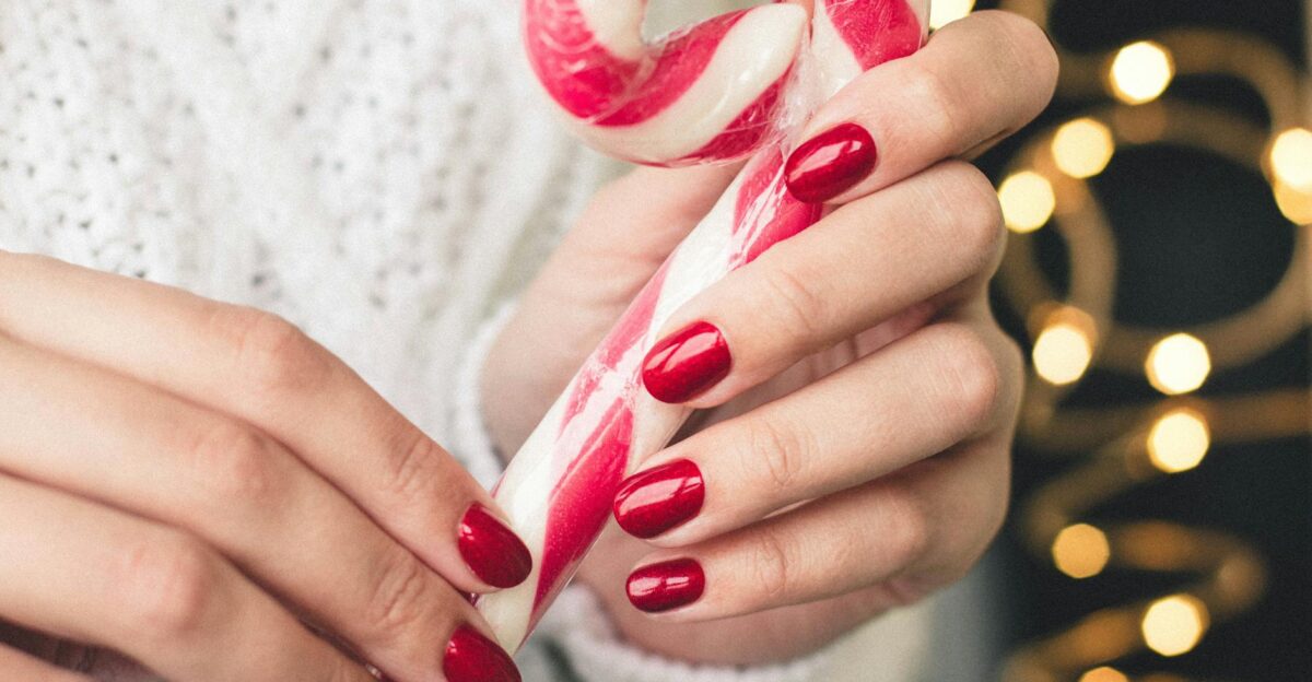 Close-up of hands with red nails holding a candy cane perfect for Christmas-themed visuals