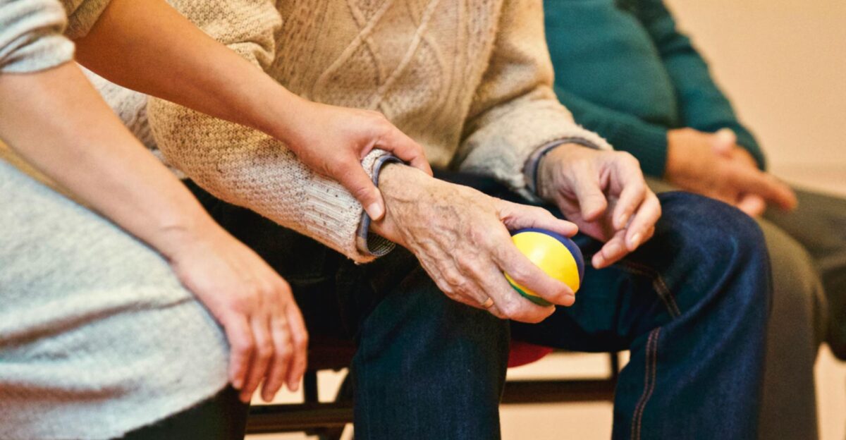 An elderly person receives support from a caregiver holding hands indoors showcasing compassion