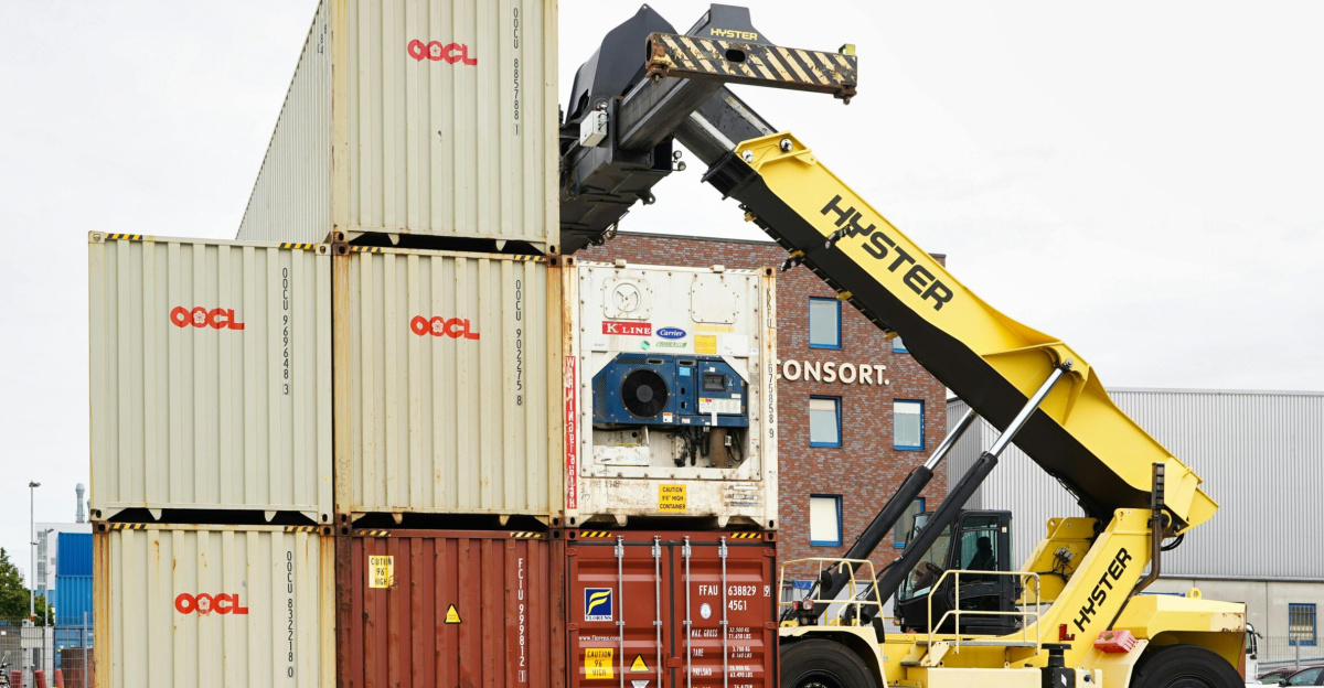 A container stacker organizing shipping containers at Hamburg port on a clear day.