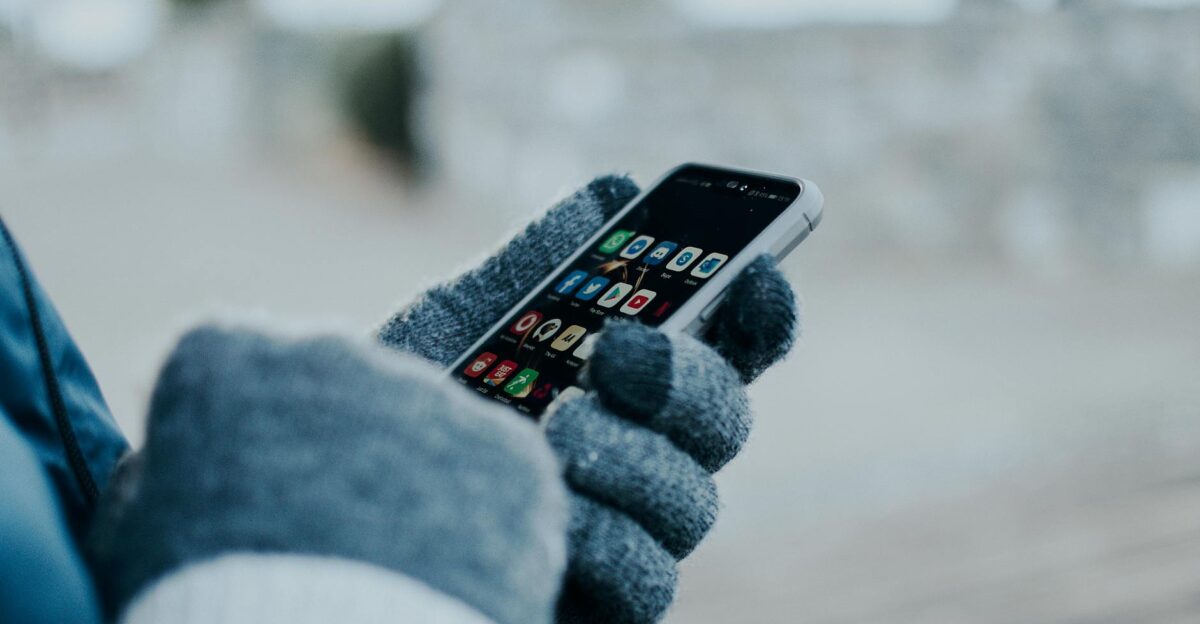 Close-up of hands using smartphone with gloves in winter showing apps on screen