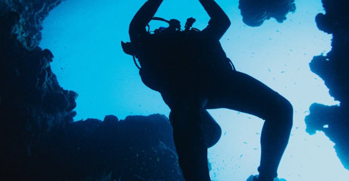 Scuba diver silhouetted against blue water while exploring an underwater cave