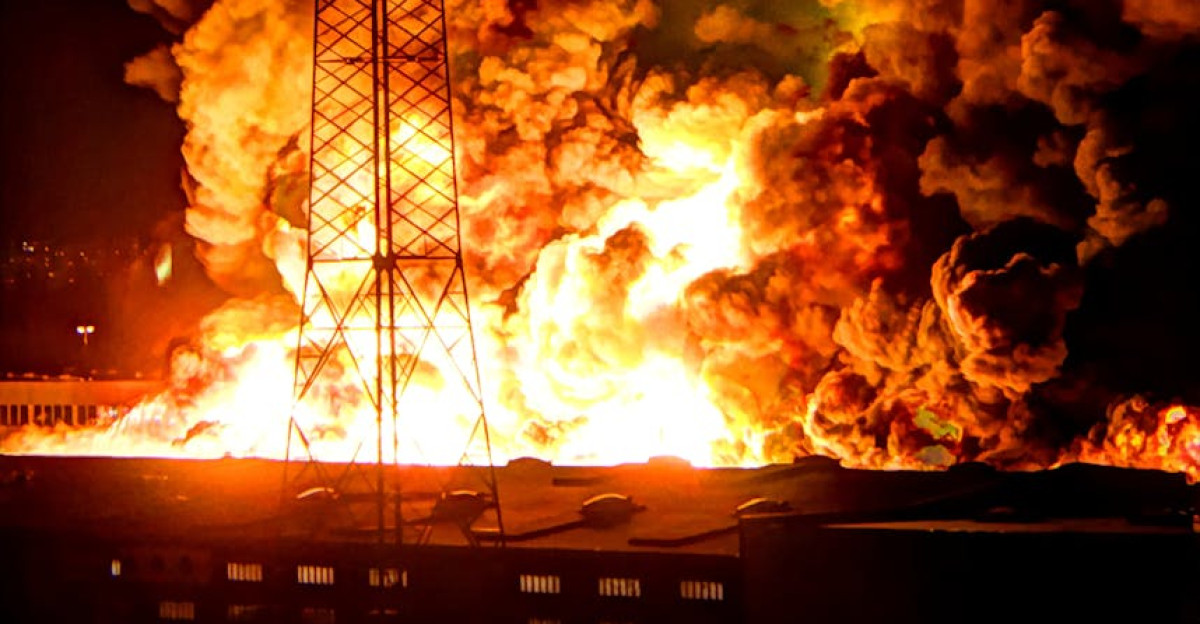 A powerful nighttime explosion at a factory with flames and smoke under power lines