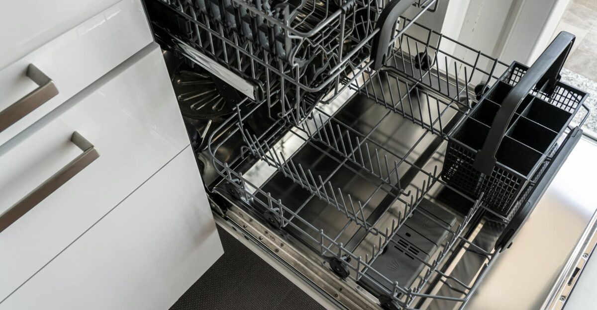 A clean and empty stainless steel dishwasher open in a modern kitchen setting