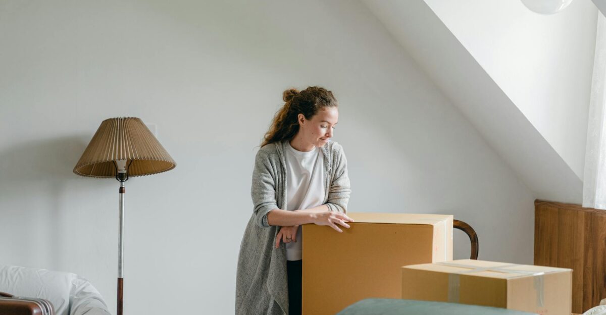Woman in a calm setting pondering on relocation with moving boxes in an attic room