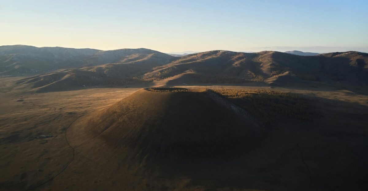 Dormant volcano in quiet desolate valley surrounded with mountain ranges in sunlight under clear blue sky
