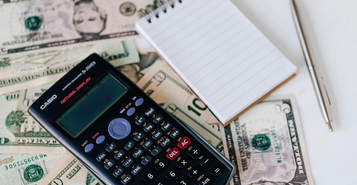 From above electronic calculator and notepad placed over United States dollar bills together with metallic pen for budget planning and calculation