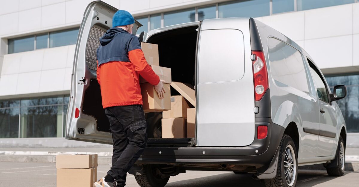 Man in colorful jacket loading cardboard boxes into a van outside an office building