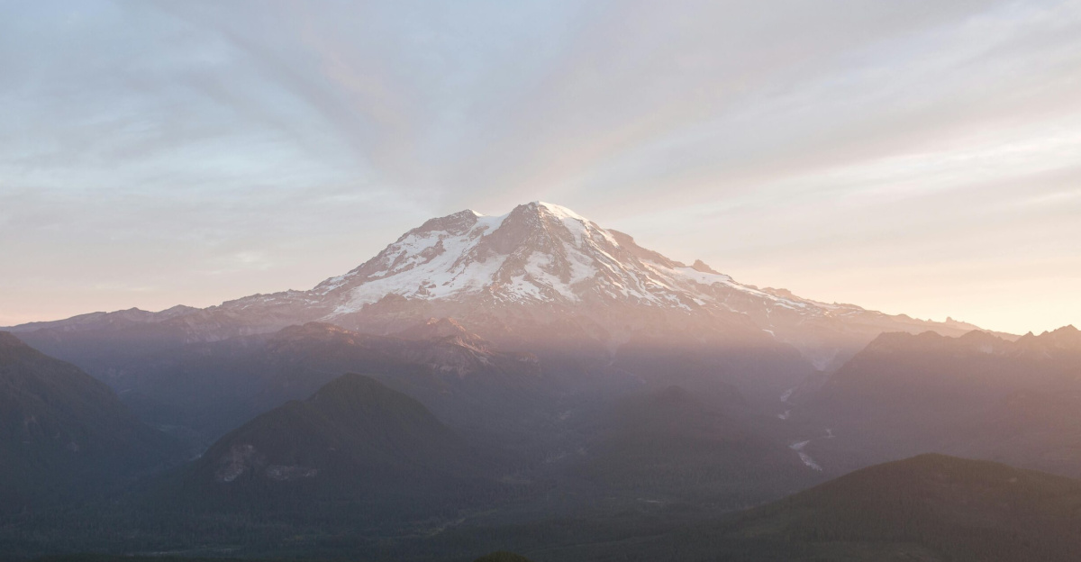 A breathtaking sunrise over Mount Rainier with snow-capped peaks and atmospheric mist.