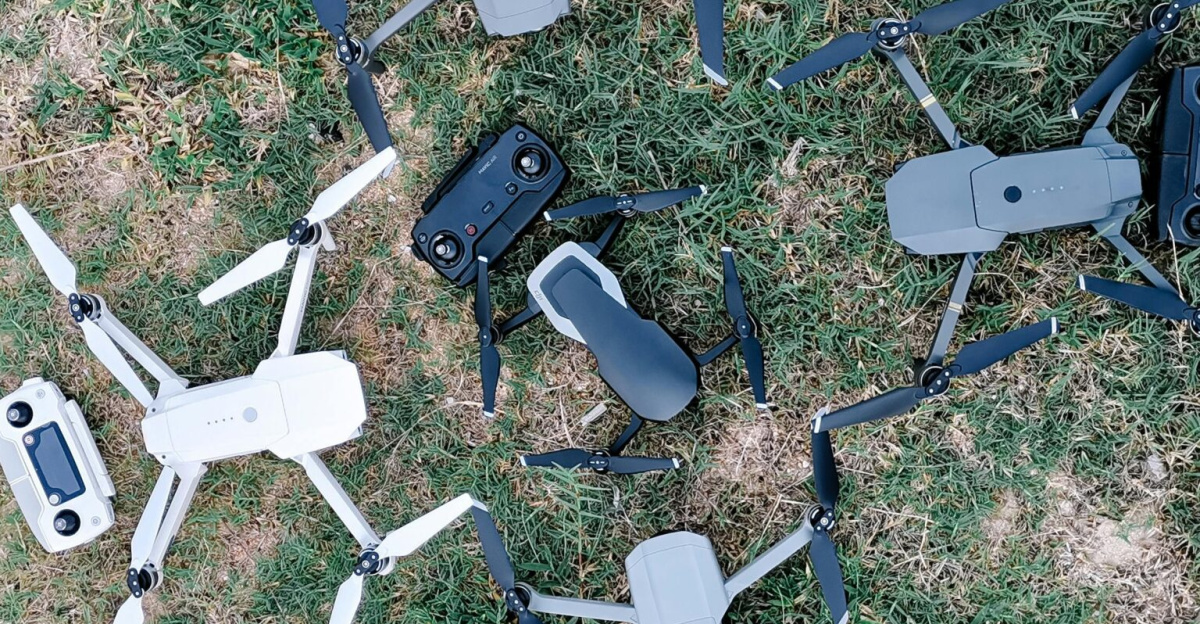 Overhead view of collection of contemporary unmanned aerial vehicles with remote controllers on grass meadow in daylight