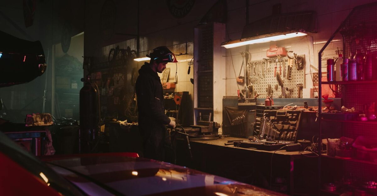 Mechanic working in a dimly lit garage workshop surrounded by tools and equipment
