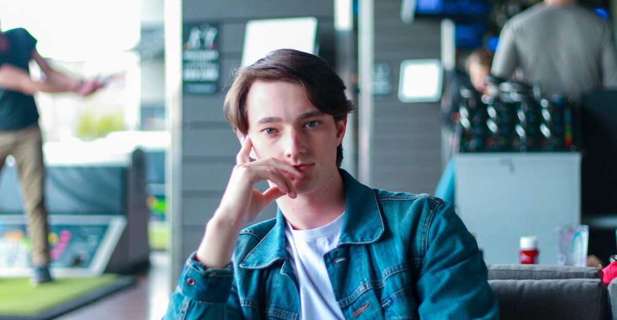 Concentrated young male employee in casual outfit sitting in modern cafe and looking at camera with hand on cheek