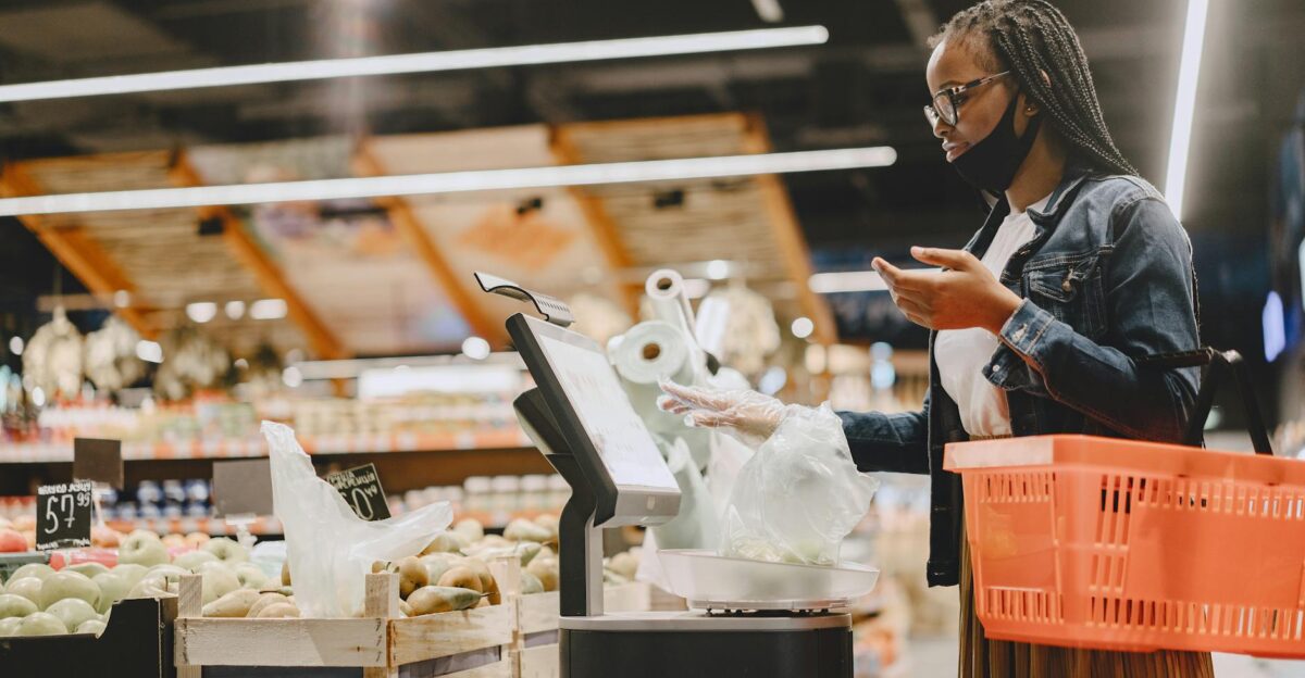 A woman with a mask shops and weighs groceries in a modern supermarket setting