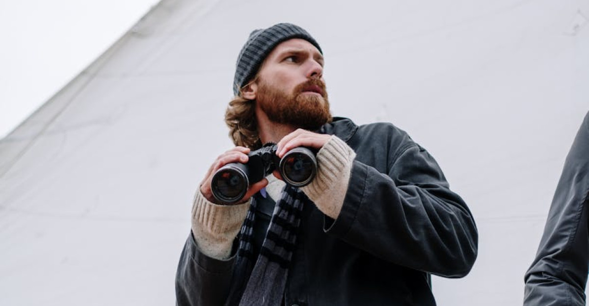 A man dressed warmly holding binoculars on a ship deck at sea