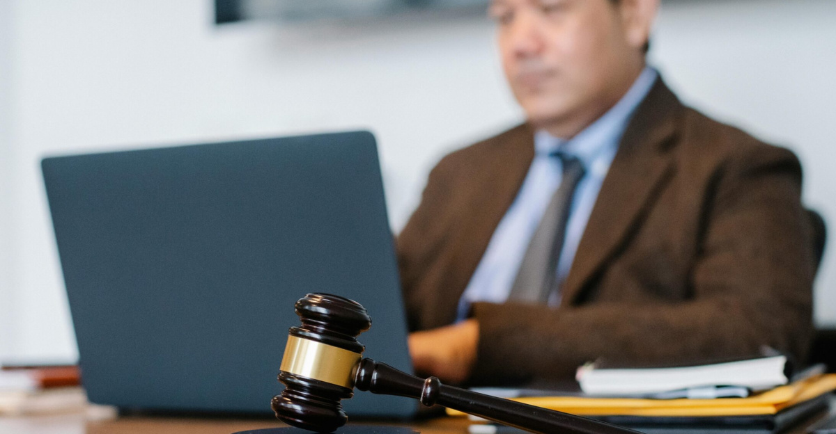 Crop concentrated Asian male judge in formal clothes sitting using modern netbook while working in law office