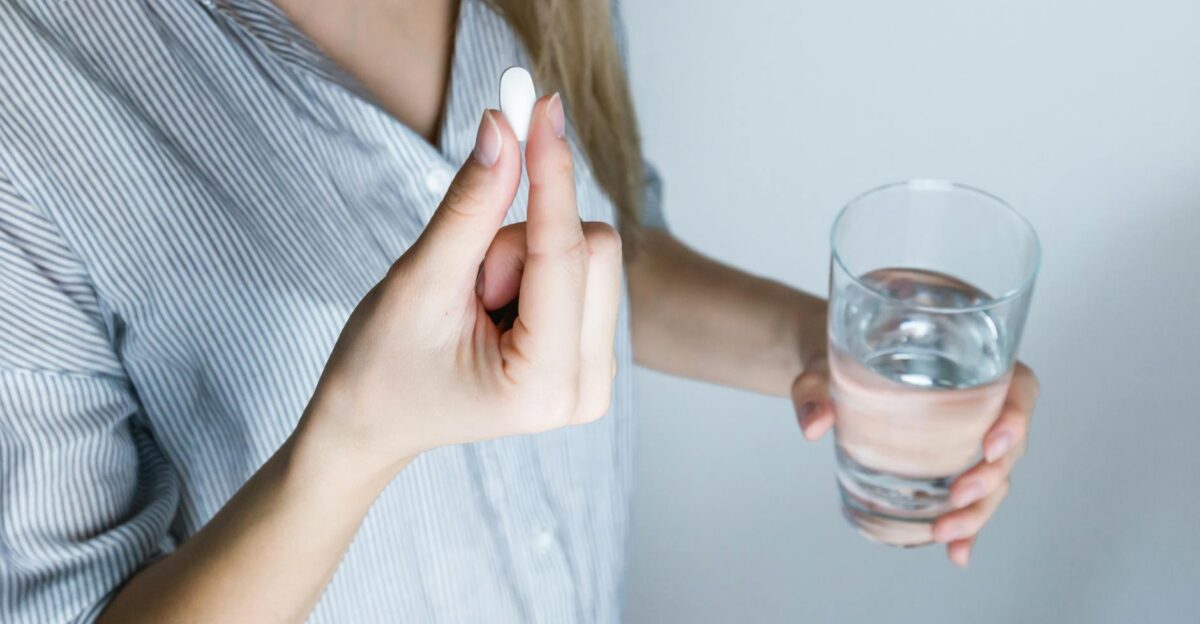 Close-up of a woman holding a pill and a glass of water ready to take medication