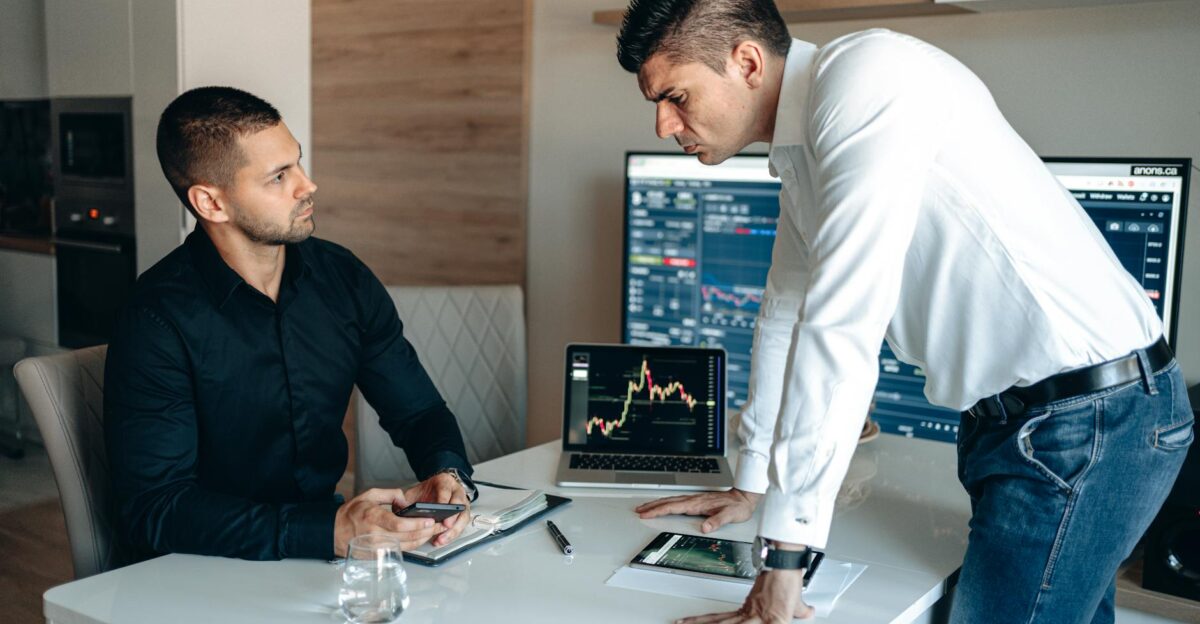 Two businessmen analyzing stock market data on laptops and tablets in an office environment