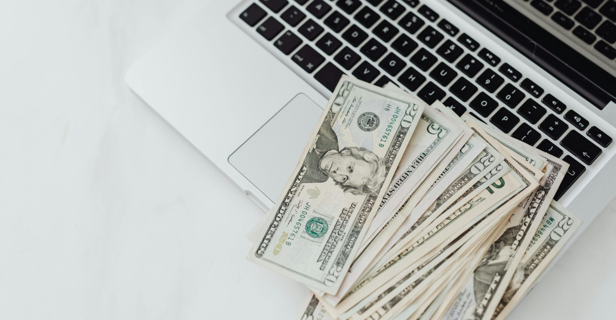 A stack of US dollar bills on a laptop keyboard representing online finance and budgeting.