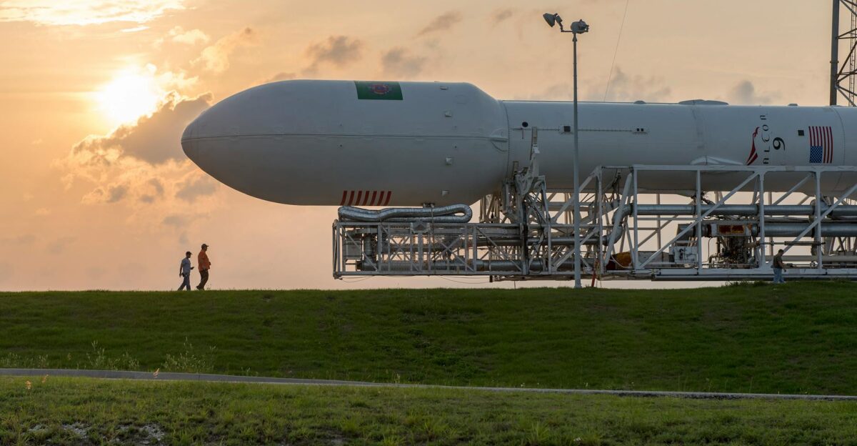 A space shuttle on a launchpad with people walking nearby at sunset