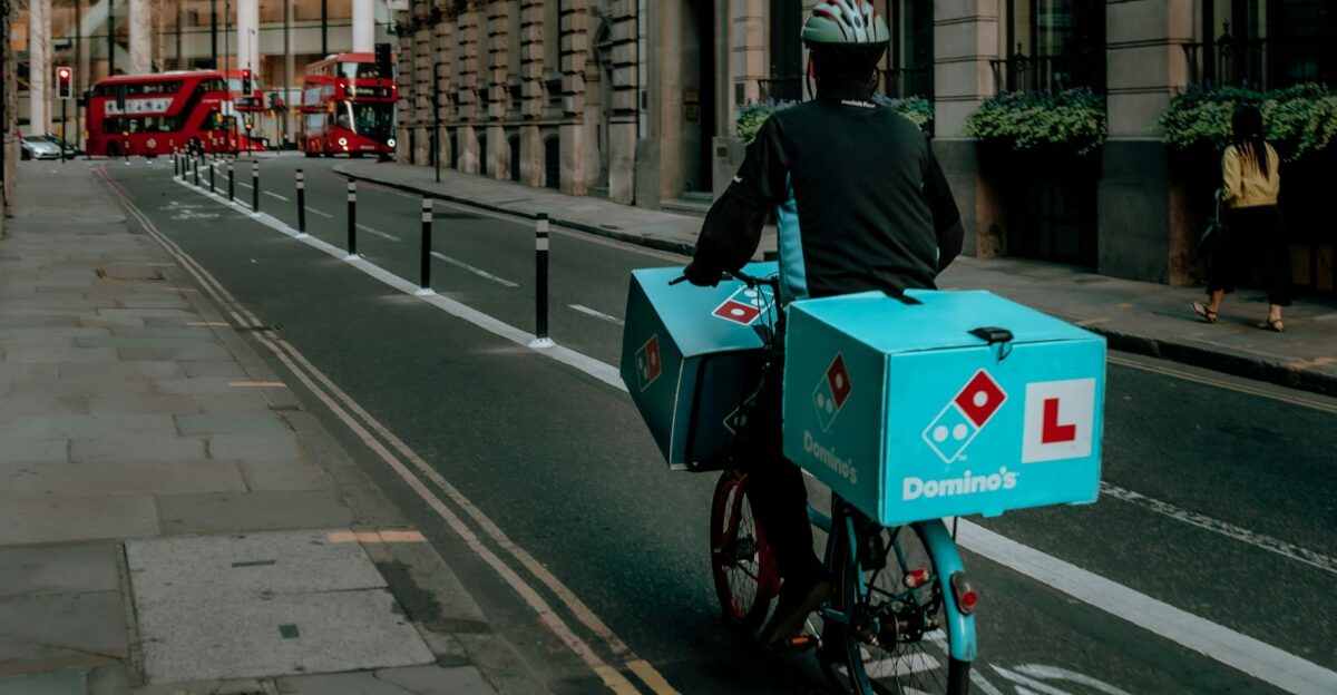 Delivery person on a bicycle in urban city with iconic red double-decker buses and historical buildings