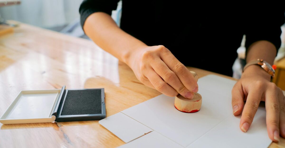 Close-up of hands stamping a document on a wooden desk indoors