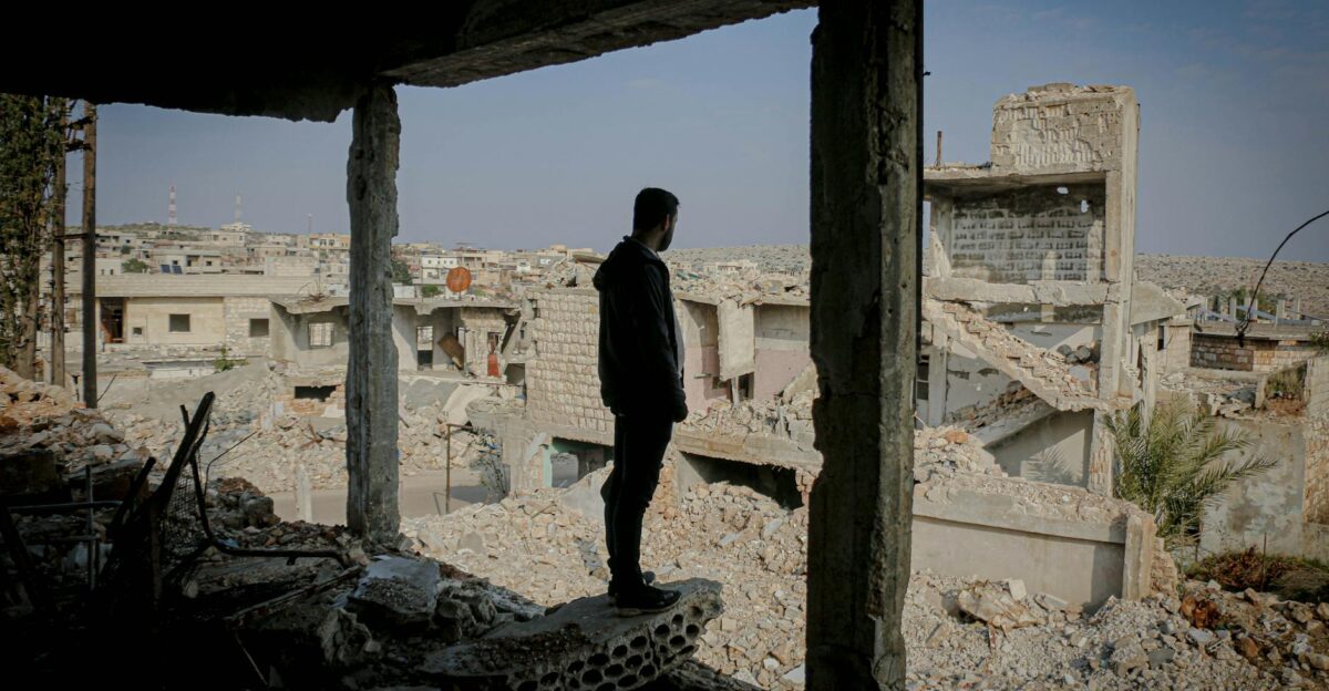 Full body side view of anonymous male standing in demolished house above remains of ruined buildings on street in poor district