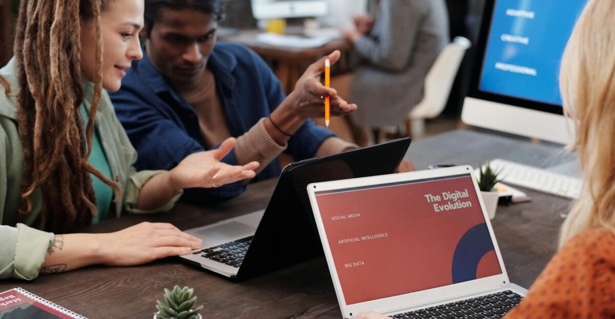 Diverse team collaborating with laptops in a modern office setting discussing digital evolution