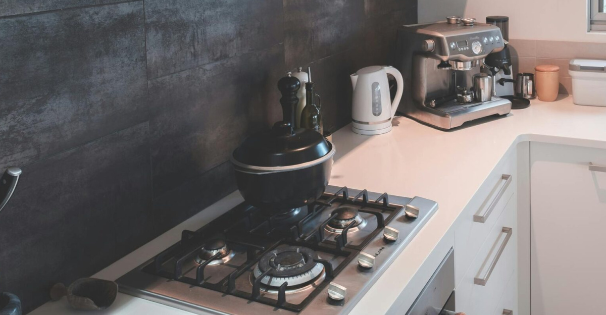 Interior of modern kitchen with white furniture and various appliances and kitchenware in light apartment