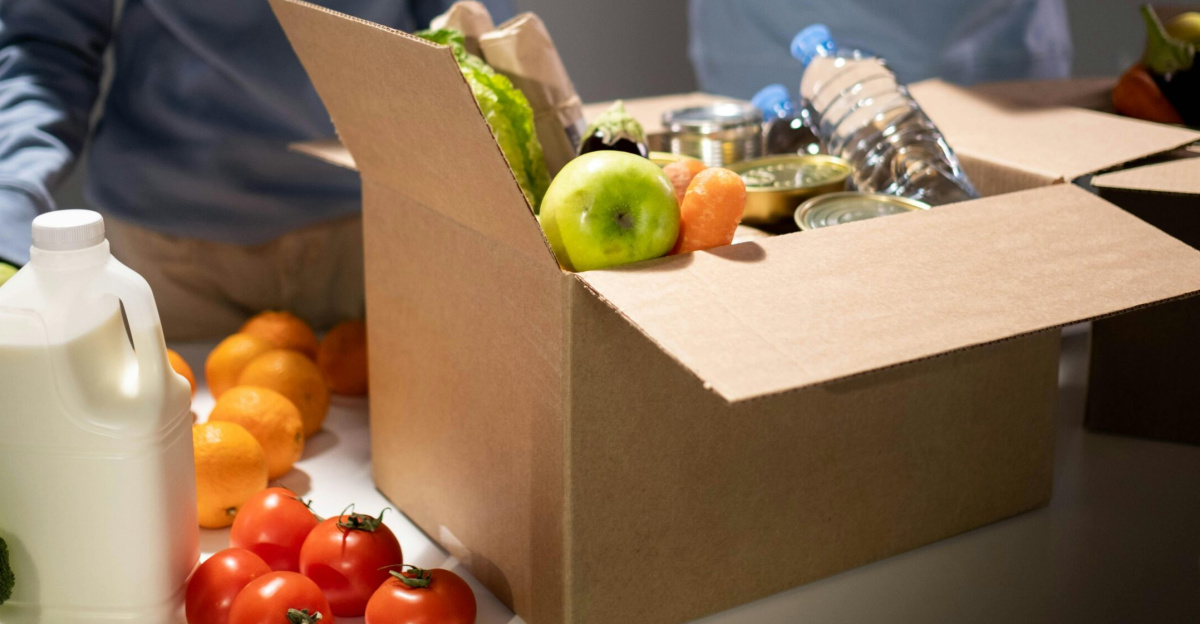 People packing a cardboard box with essentials like fruits, vegetables, and bottled water for charity.