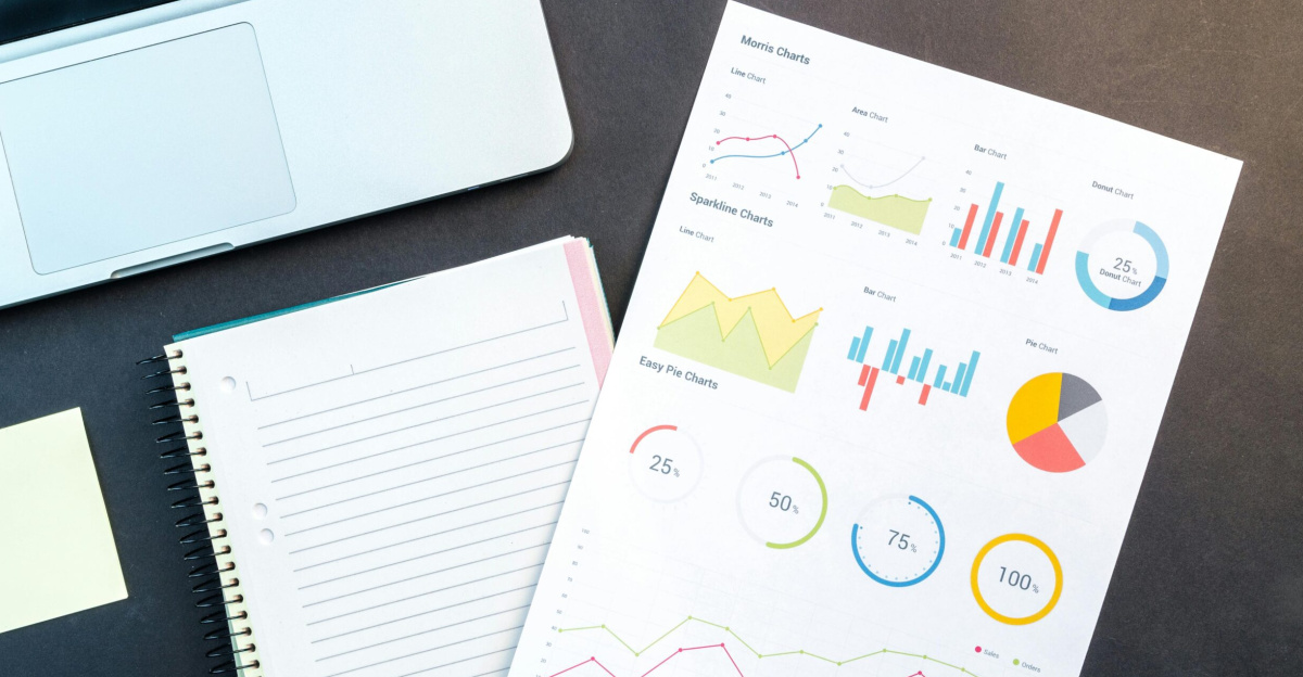 Flatlay of business report with colorful charts, a notebook, and a laptop for data analysis on a desk.