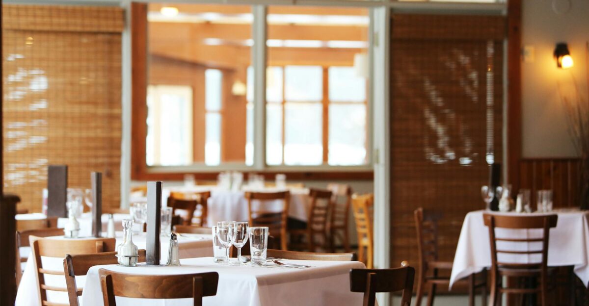 A serene restaurant interior with wooden chairs and tables set with glasses ready for dining