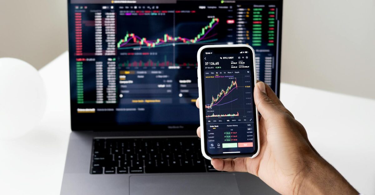 Person checking stock market graphs on laptop and smartphone focusing on financial data