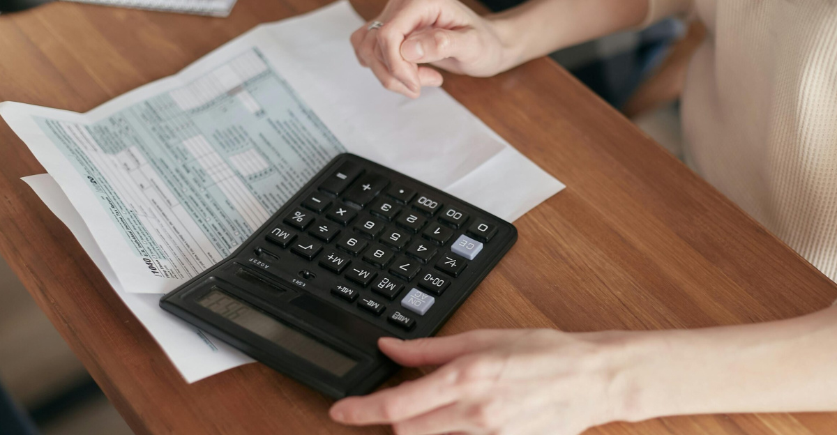 Focused individual using calculator to manage personal finances at wooden desk.
