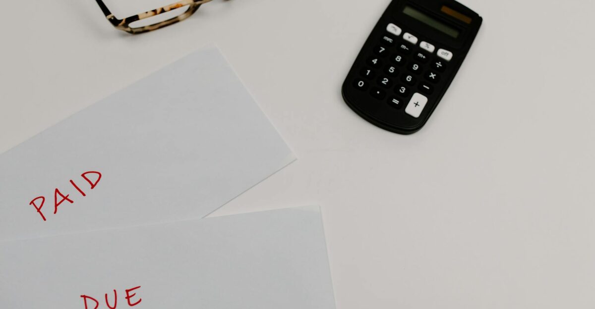 Top view of financial papers labeled Paid and Due beside a calculator and glasses