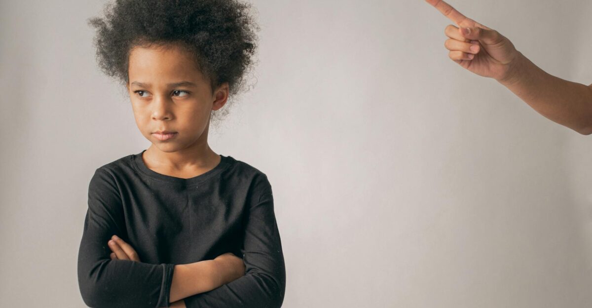 Young girl with arms crossed looks displeased as finger points conveying discipline