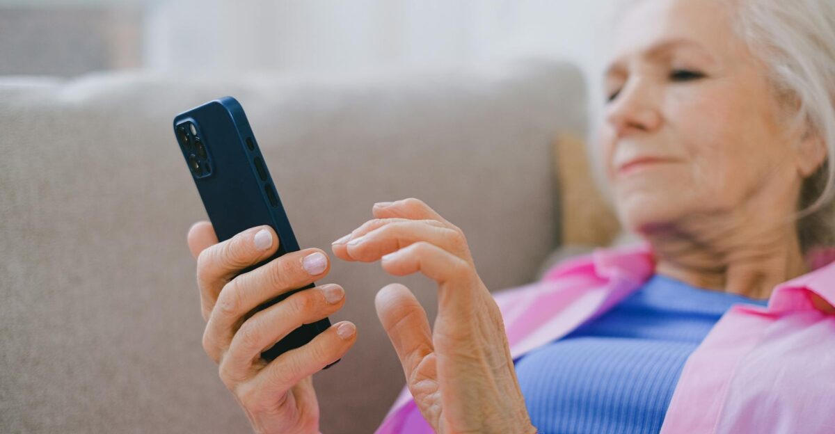 Elderly woman in pink shirt using smartphone on a couch at home engaged in technology
