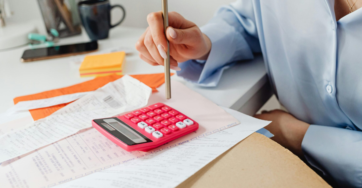 A woman is calculating expenses using a calculator and papers at her desk.