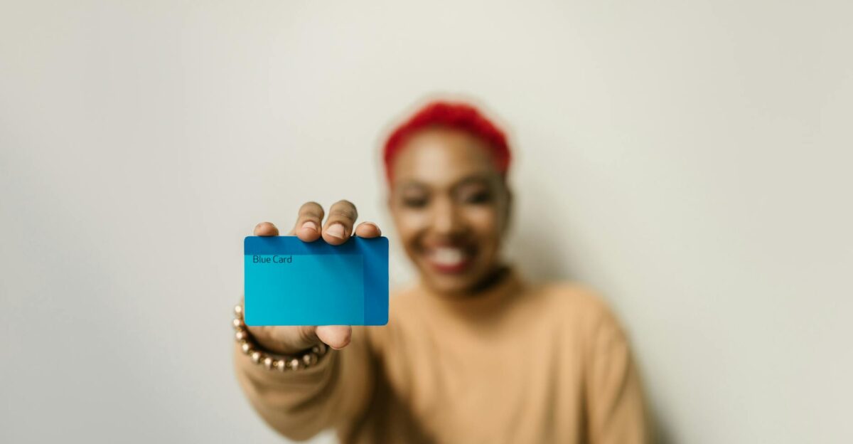 A cheerful woman with red hair displays a blue card against a neutral background focused on the card