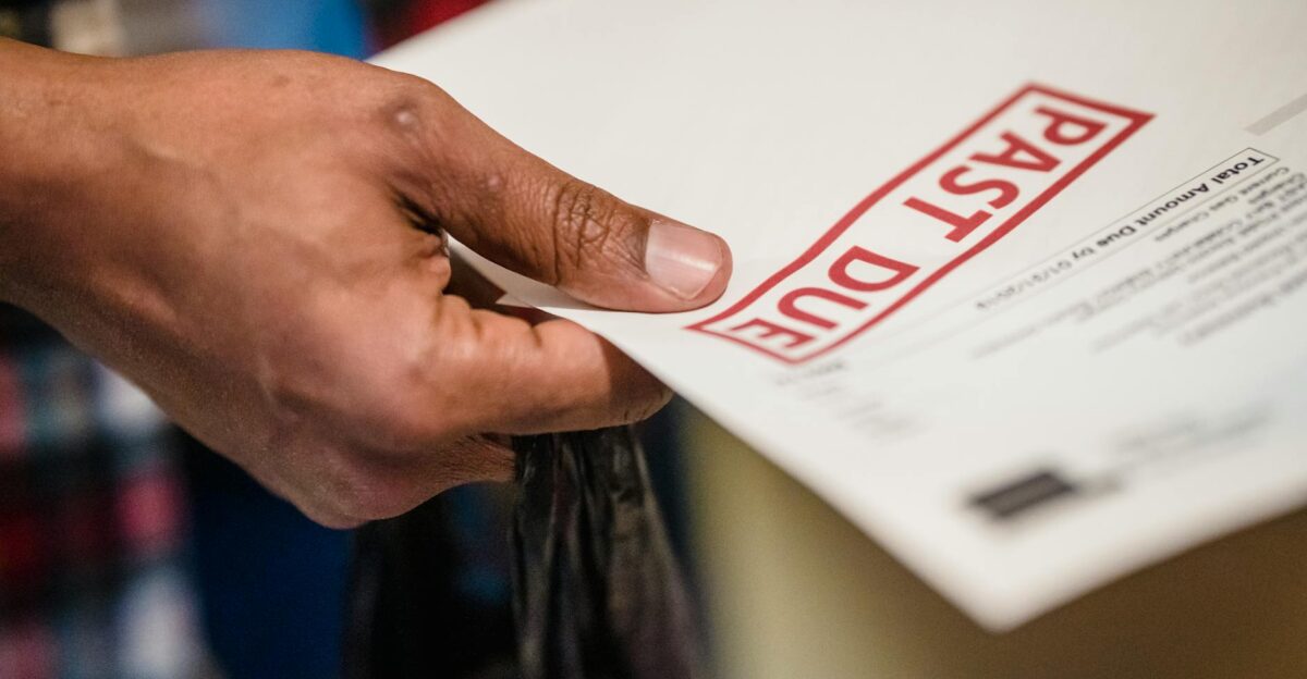 A close-up of a hand holding a document with a Past Due stamp highlighting financial urgency