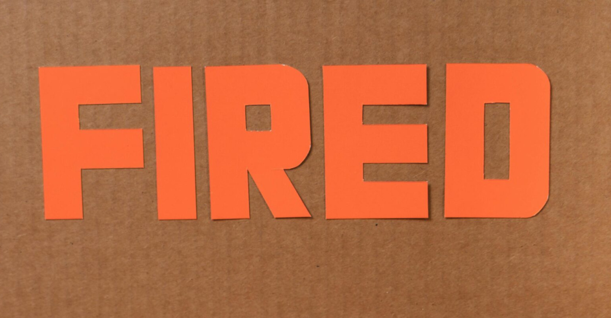 Close-up of a cardboard box labeled FIRED on a wooden table with crumpled papers.