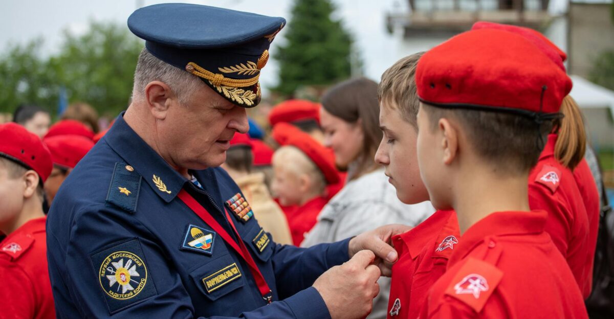 A Russian officer in uniform pinning a badge on a young recruit during an outdoor military ceremony