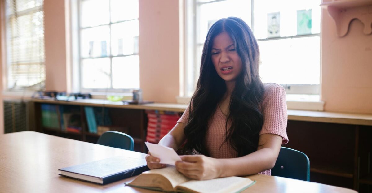 A woman in a pink top appears frustrated while reading in a library environment