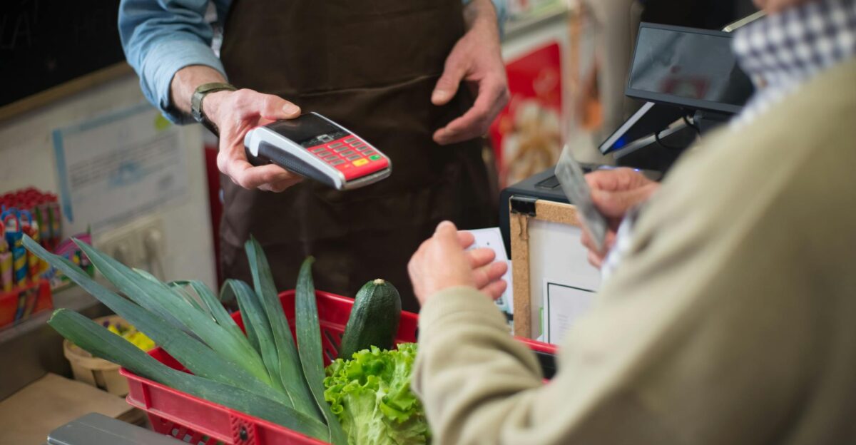 Close-up of customer paying for groceries with produce at a store checkout counter