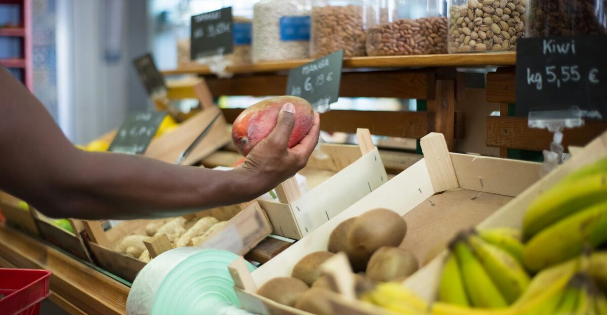 Close-up of a hand choosing a mango among fresh produce at a market in Portugal