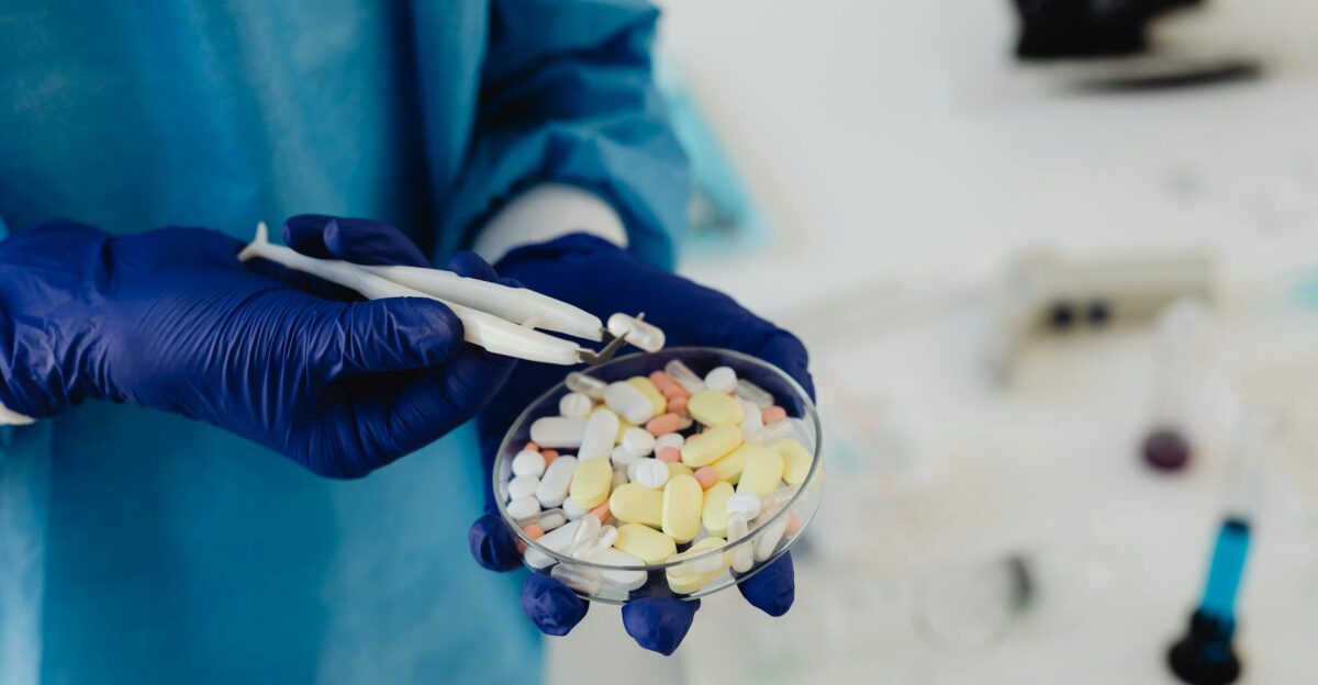 Scientist in gloves using tweezers to handle assorted pills in a petri dish